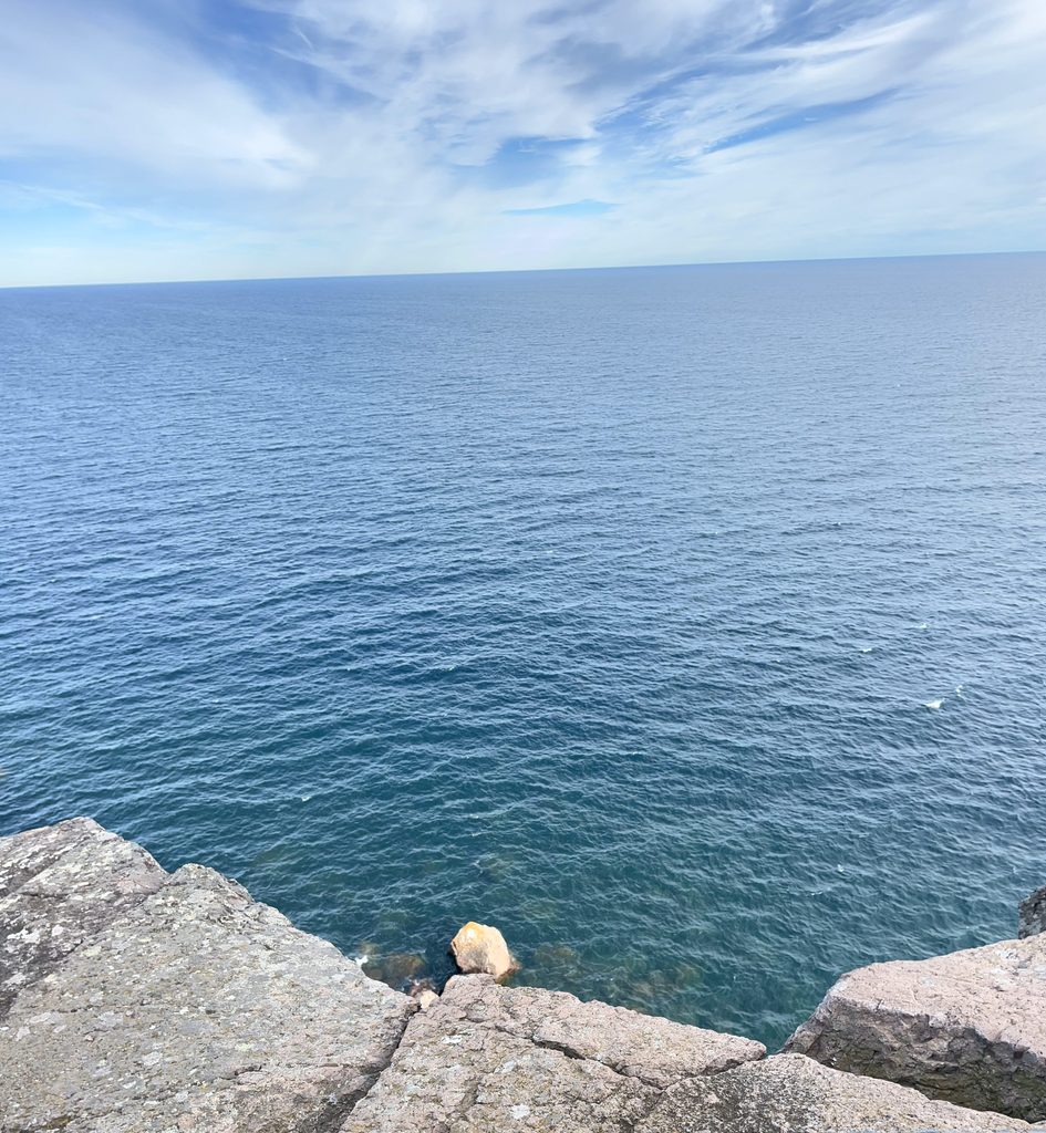 Clear blue lake water stretching toward the horizon, viewed from a rocky shoreline.